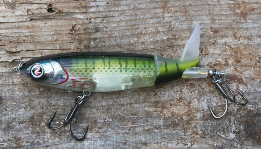 Jointed prop-style topwater bass lure with a rotating tail blade on weathered wood