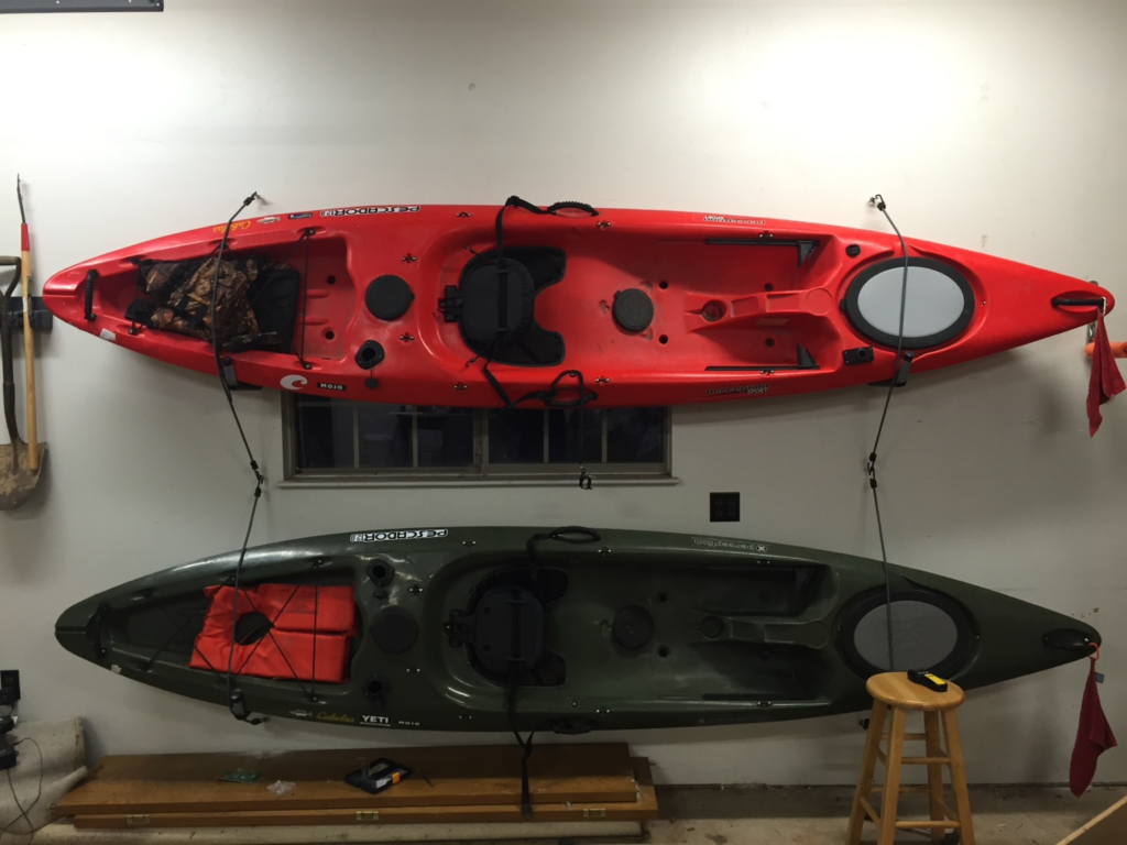 Two fishing kayaks stored horizontally on a garage wall
