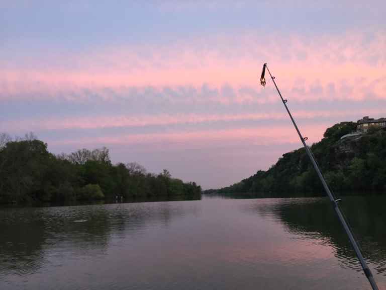 Fishing rod over calm water at dusk with a soft-plastic lure hanging from the line
