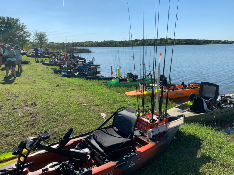 Lineup of rigged fishing kayaks along the shoreline at a bass fishing event